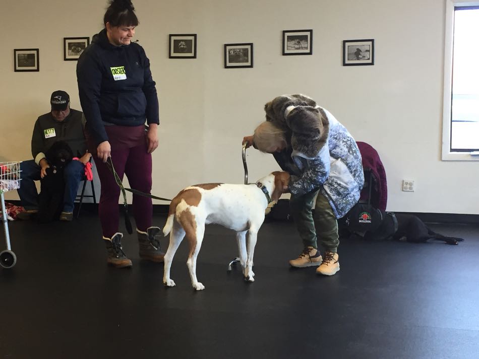 a white and tan dog greets a woman holding onto a cane.