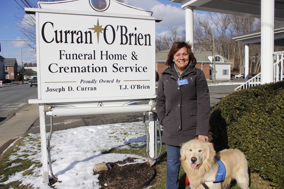 Golden Retriever Mac and his teammate stand outside by the Curran-OBrien Funeral Home sign.