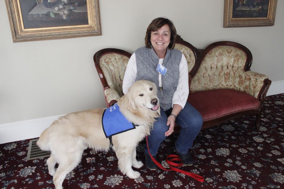 Bright Spot Therapy Dog Mac wears his blue therapy dog vest as he and teammate Mary O'Brien sit on a sofa in the the funeral home foyer.