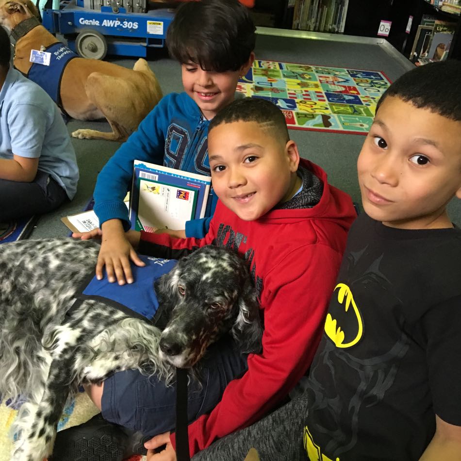 three children sit on the floor next to their Reading Buddy dog Lily, a blue Belton English Setter