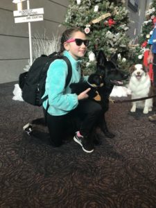 girls wearing sunglasses knees and hugs a black dog