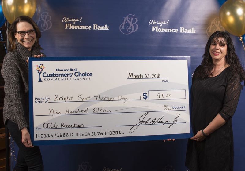 two women hold a replica of a giant check given to Bright Spot Therapy Dogs