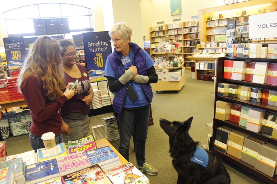 volunteer with black dog stands talking to a person shopping in the store